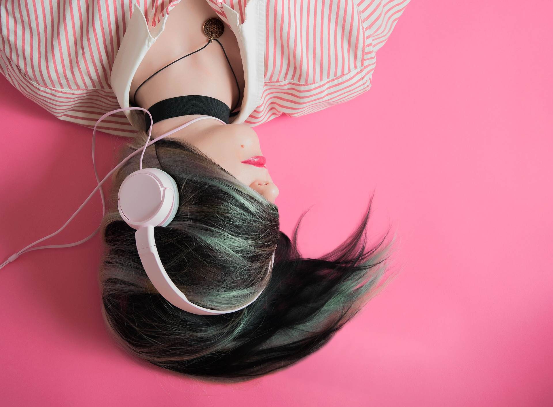 Ein Mädchen trägt Kopfhörer und liegt auf einem Hintergrund in pink